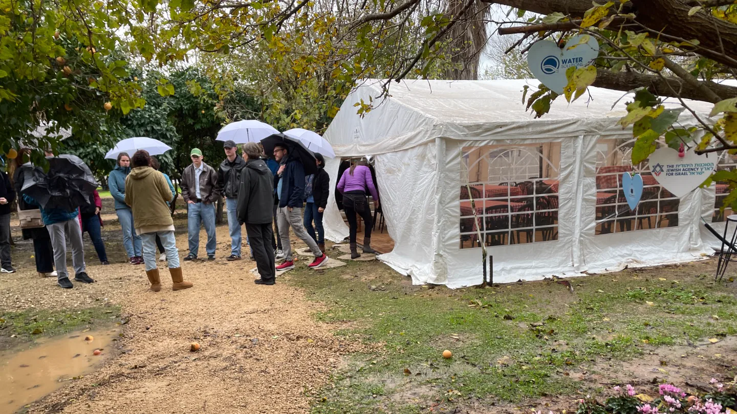 Menschen mit Regenschirmen vor einem weißen Zelt in einem Garten.